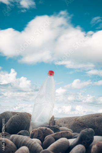 Plastic bottle with red cap among rocks on a polluted beach