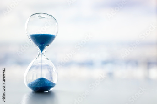 Hourglass on desk by window in office with city skyline background concept for business time management and schedule