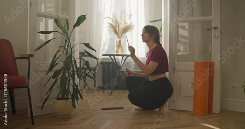 A brunette girl in a Red T-shirt lights incense before starting meditation at home