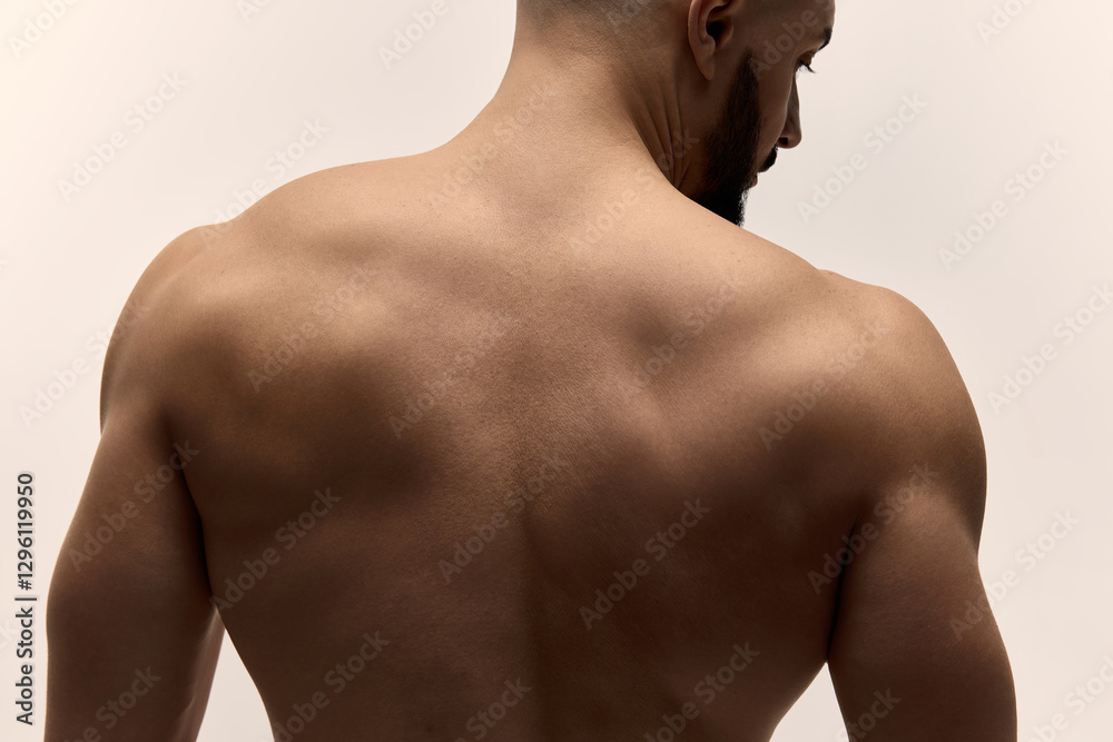 Fototapeta premium Cropped image of fit man upper back muscles posing shirtless confidently highlighting smooth skin texture and toned muscular physique against white studio background. Male body care and beauty.