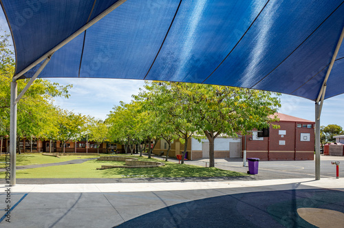 View from under a blue shade sail in a primary school campus with neatly maintained green spaces.A sheltered outdoor learning or play area typical of Australian educational facilities.