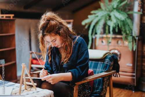 Fotografie Young woman is deeply absorbed in her painting activity within a cozy indoor space
