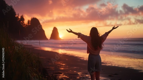 A woman stands on a beach with her arms outstretched, looking out at the ocean