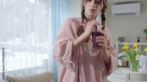 A teenage girl in a pink knitted sweater is drinking a freshly blended berry smoothie from a glass. Healthy nutrition, homemade drinks, and a balanced diet for kids and teenagers