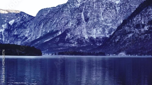 Scenic winter landscape featuring snow-covered mountains and a tranquil lake reflecting the rugged peaks, with a forested shoreline in view.