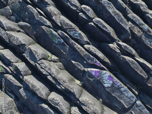 Close up of weathered gray rock surface, revealing diagonal stratification and vibrant lichen patches creating rugged, textured geological landscape