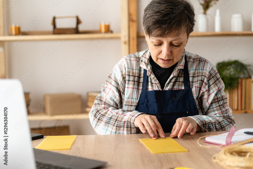 A craftswoman watching a video tutorial or training course on making wax candles DIY rolls a candle on a table in home workshop A craftswoman watching a video tutorial or training course on making wax candles DIY rolls a candle on a table in home workshop