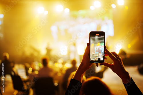 unrecognizable faces. Female hands with a smartphone in their hands shoot a video of a concert on stage.