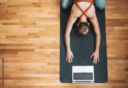 Top view of woman practicing yoga on yoga mat with laptop.