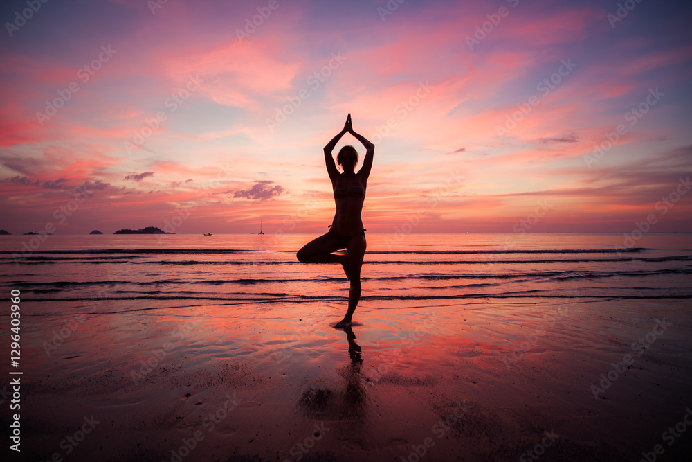 The silhouette of a woman standing in meditation on the shoreline of a subtropical beach at sunset.