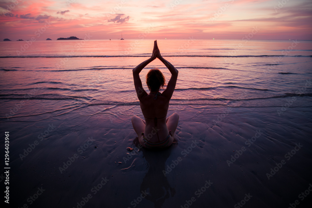 A woman meditating on the shoreline of a subtropical beach during a beautiful sunset.