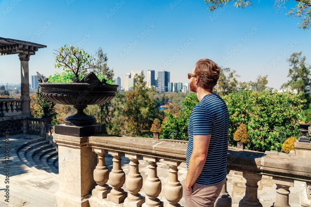 A tourist man standing at a terrace overlooking the Chapultepec Forrest and Mexico City skyscrapers