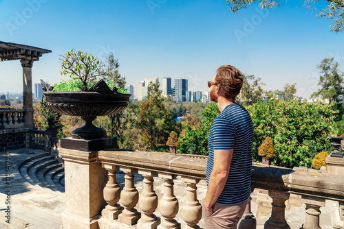 Obraz na płótnie A tourist man standing at a terrace overlooking the Chapultepec Forrest and Mexico City skyscrapers w salonie