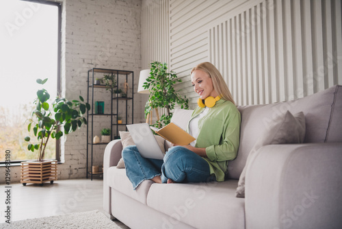 Young woman relaxing on a sofa while reading and using a laptop in a bright modern apartment