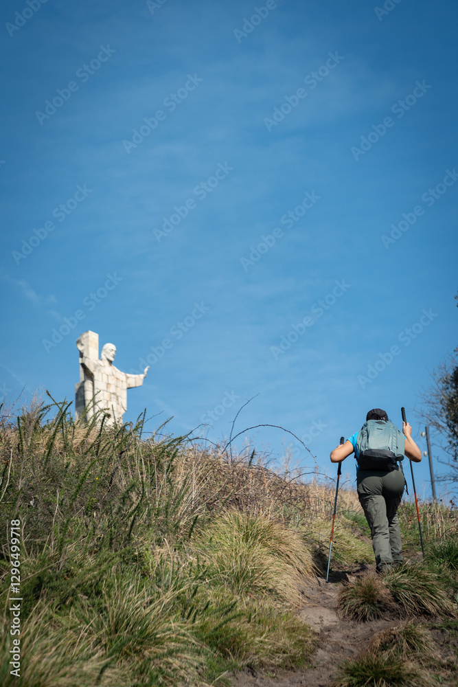 Obraz premium Woman climbing Naranco Mountain in Oviedo, Spain, finds statue of Christ the Redeemer at the top.