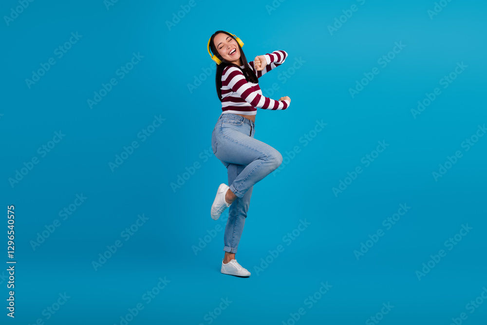 Obraz premium Cheerful young woman wearing headphones dancing with joy on a vibrant blue background