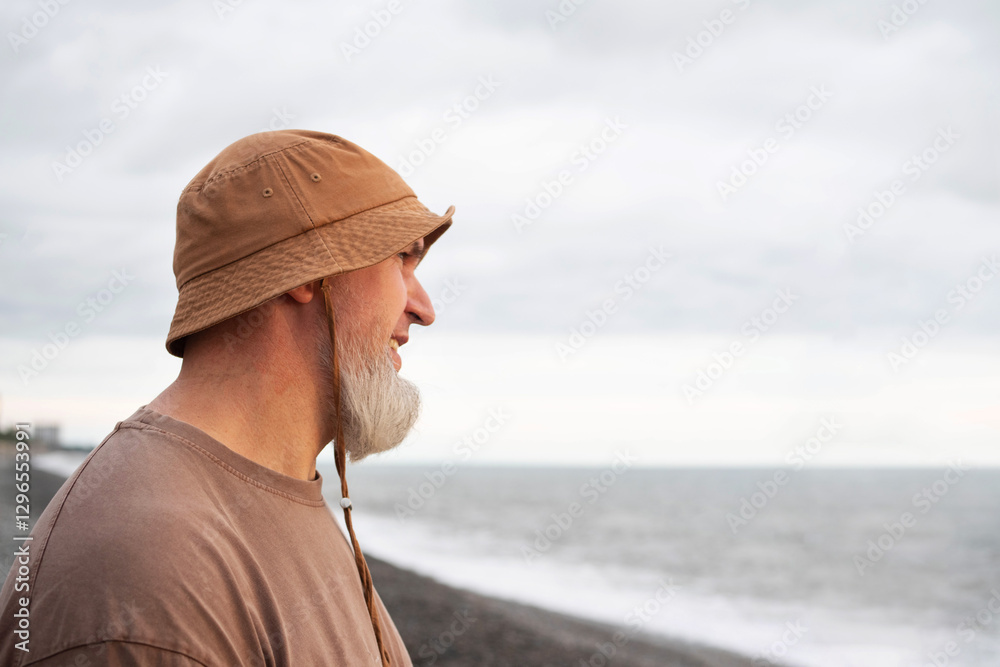 Lonely man with grey beard in hat looking into the distance at sea on cloudy autumn day on beach Lonely man with grey beard in hat looking into the distance at sea on cloudy autumn day on beach