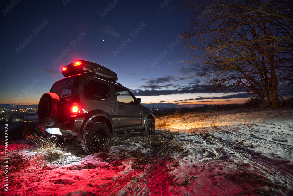 an old all-terrain vehicle stands on the top of the mount, In the background are the lights of the city, a late sunset. Glowing running lights and red stops. Stars in the sky. Copy space