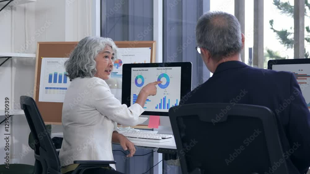 Business professionals reviewing financial analytics, discussing strategy while examining data charts on computer screen inside sleek corporate office setting