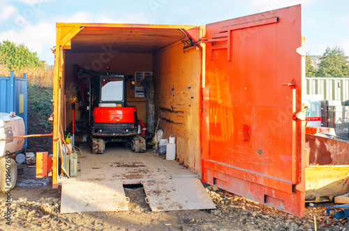 Obraz na plátne Construction site storage container houses a compact excavator ready for use on