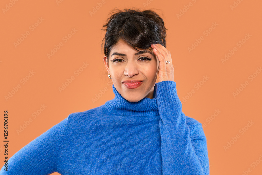 Woman in blue sweater stands against brown background, showcasing thoughtful expression while resting hand on temple Woman in blue sweater stands against brown background, showcasing thoughtful expression while resting hand on temple