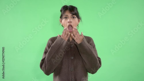 Woman in brown sweater covering her mouth with surprise in front of a green screen background during a reaction moment