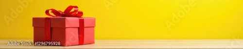 Gift box with red ribbon tied to a wooden table against a sunny yellow background, ribbon, yellow, present
