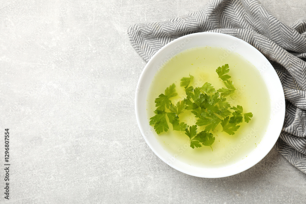 Tasty chicken bouillon with parsley in bowl on grey table, top view. Space for text Tasty chicken bouillon with parsley in bowl on grey table, top view. Space for text
