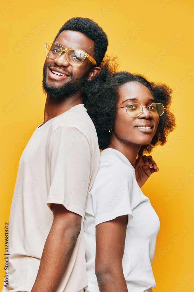 Obraz premium Two smiling models with glasses in casual outfits against a vibrant yellow background, showcasing a youthful and positive vibe