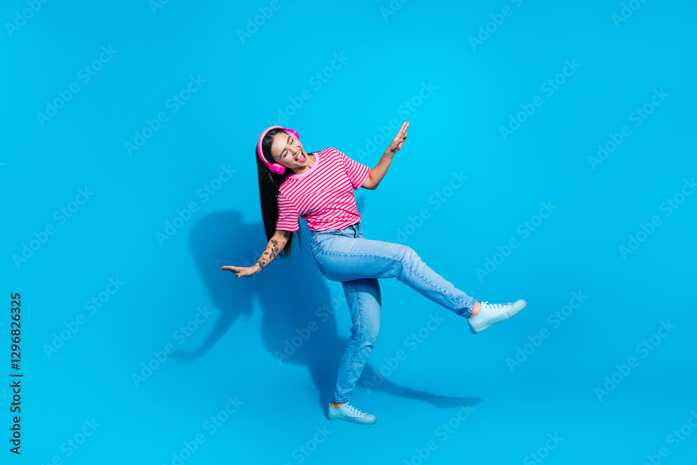Obraz premium Woman in casual outfit dancing with headphones against vibrant blue background promoting lively and cheerful lifestyle