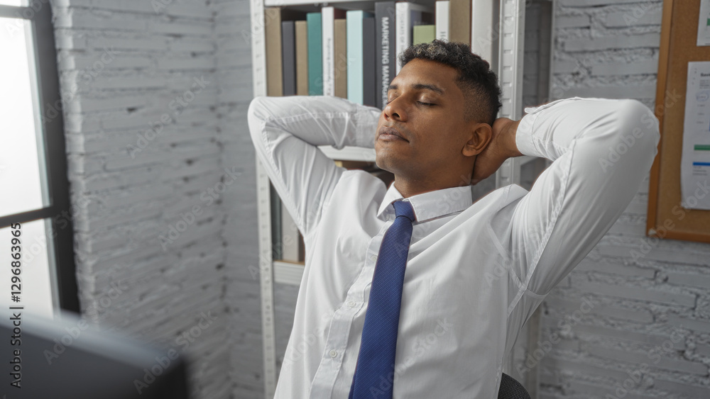 Fototapeta premium Handsome man relaxing in office indoors with hands behind head after a long workday