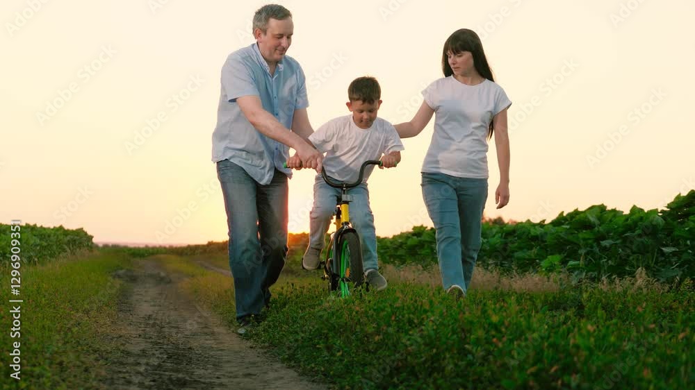 Mom puts hand on son learning riding bicycle with help of father on vocation. Dad holds handlebar of bicycle while son pedals near mom. Mum happy seeing son enjoying riding bicycle at twilight Mom puts hand on son learning riding bicycle with help of father on vocation. Dad holds handlebar of bicycle while son pedals near mom. Mum happy seeing son enjoying riding bicycle at twilight