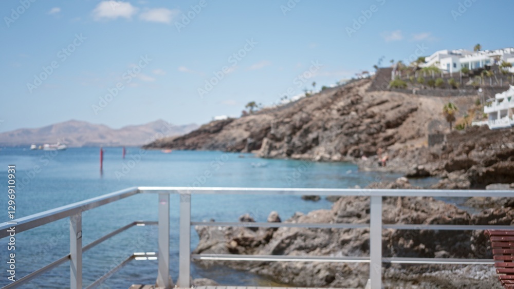 Naklejka premium Blurred coastal view in lanzarote, canary islands, showing rocky shoreline and distant boats against a clear blue sky