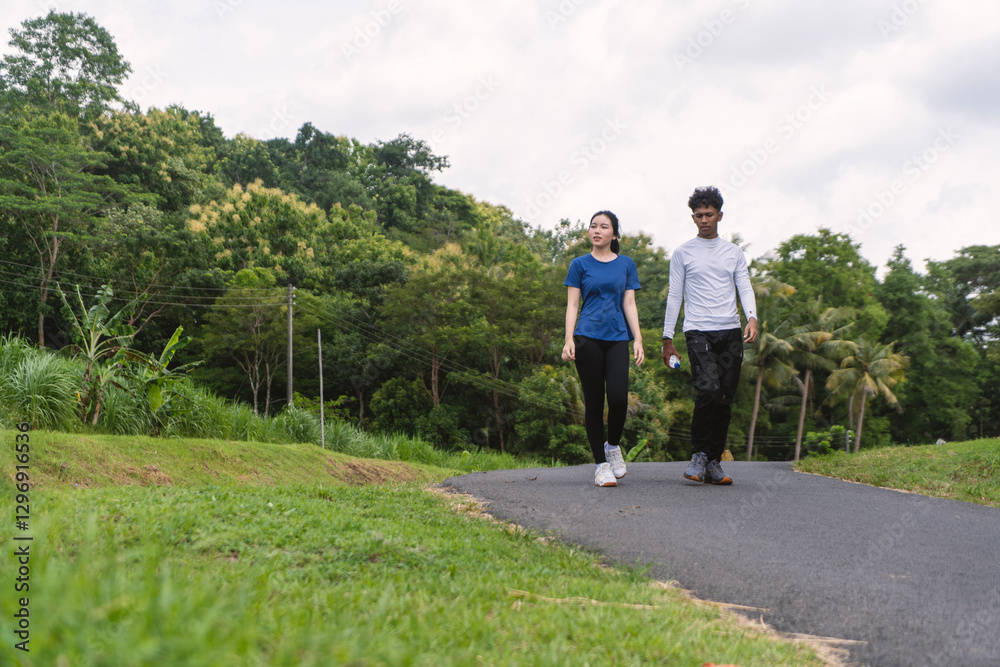 Fototapeta premium active young asian couple holding water bottle while walking exercise at rural area