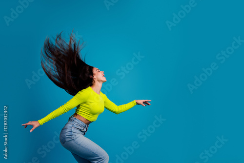 Dynamic portrait of a young woman with flowing brunette hair, wearing a bright yellow top, expressive pose against a blue background photo