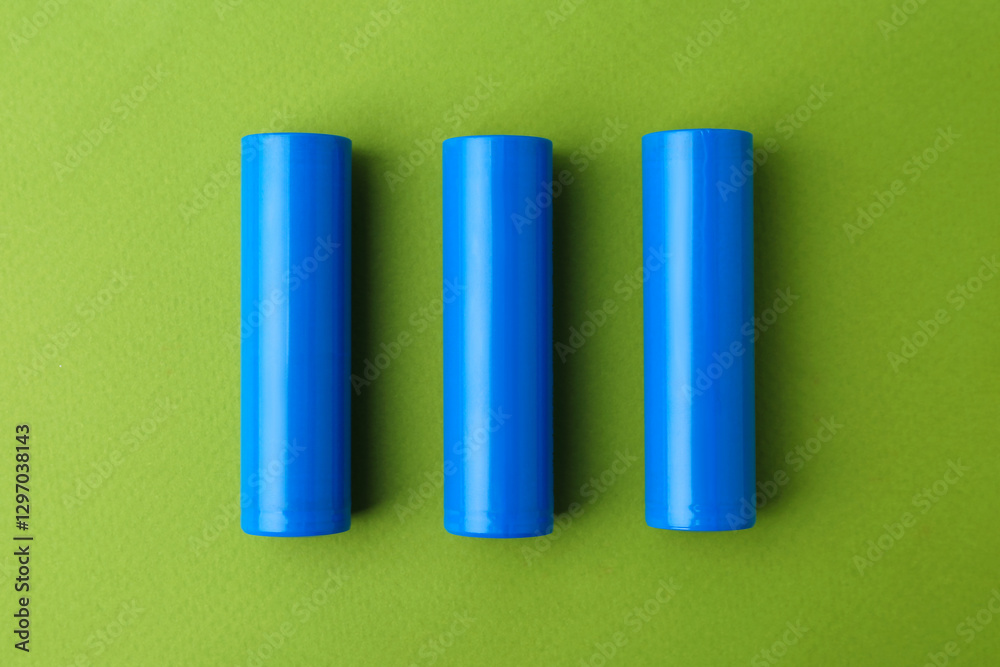 Fototapeta premium Three AA cell batteries on green background, top view