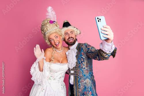 Couple in period costumes taking selfie against pink background at themed party photo