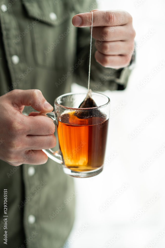 Person Holding Mug with Hot Tea Bag in Hand Over Glass Cup of Tea on Light Background Person Holding Mug with Hot Tea Bag in Hand Over Glass Cup of Tea on Light Background