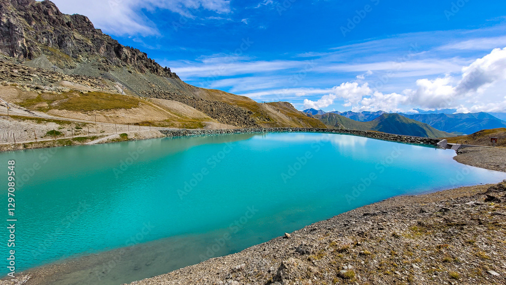 Fototapeta premium Panoramic view of the alpine lake with turquoise water, surrounded by mountain peaks, against the backdrop of the sky with light white clouds.