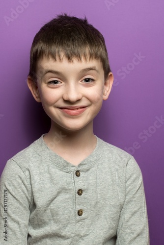 Wallpaper Mural Joyful young boy in a gray sweater with a bright smile against a purple background, perfect for childhood, happiness, and positive expression themes in imagery. Torontodigital.ca