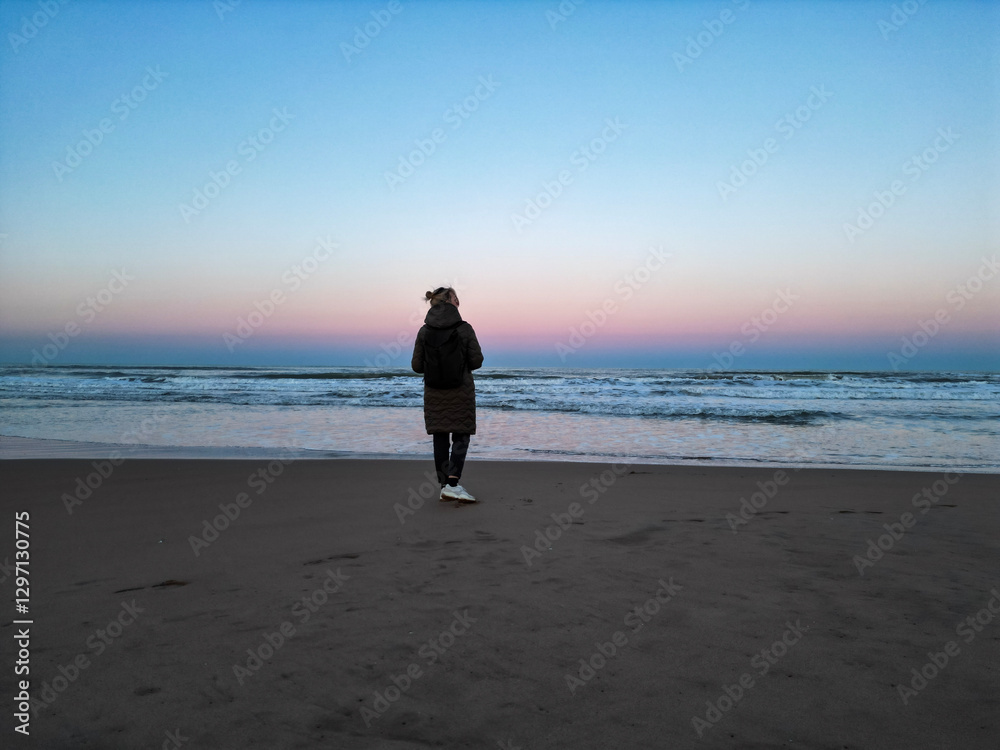 Serene Beach Sunset with Person Facing the Ocean in Playa del Grao de Gandia, Spain Serene Beach Sunset with Person Facing the Ocean in Playa del Grao de Gandia, Spain
