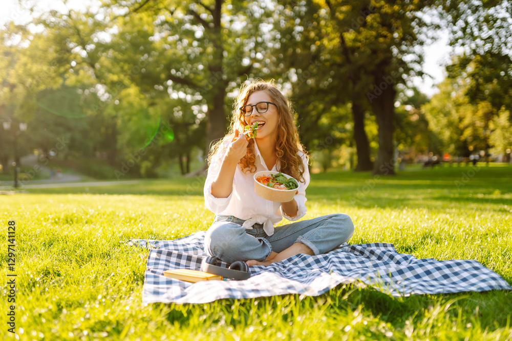 Young woman in glasses eating fresh salad sitting on blanket in sunny park. Beautiful woman enjoying lunch outdoors. Healthy eating, leisure concept. Lifestyle.
Young woman in glasses eating fresh salad sitting on blanket in sunny park. Beautiful woman enjoying lunch outdoors. Healthy eating, leisure concept. Lifestyle.