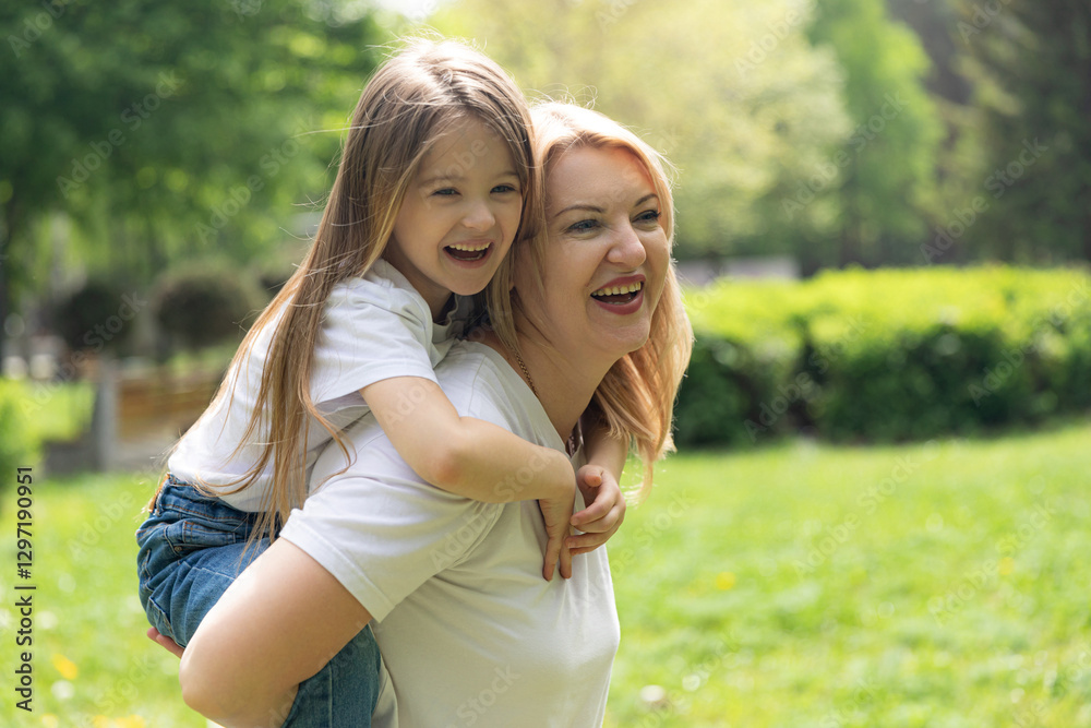 Fototapeta premium Happy laughing mother having fun with her daughter outdoor. Young woman with her little kid hugging at park. Family and love concept. High quality photo. Copy space