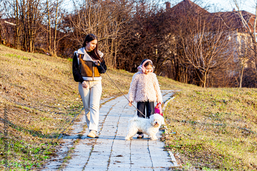 Fototapeta premium The picture was taken in a very beautiful park that was just now turning green and the sun was shining brightly. The girls were playing with their white dog, and they were very happy.