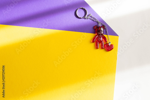 Shiny red keychain in the form of a bear and heart on a colored background