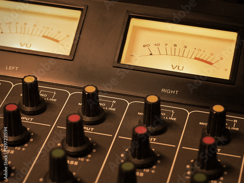 Detail of an analog studio mixer. Professional audio console with illuminated VU meters and knobs. Ideal for sound engineering, music production, or live radio show broadcasting and podcasts