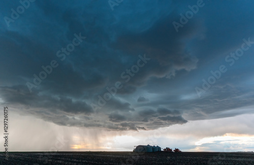 Canvas-taulu Dramatic supercell thunderstorm looming over a farm at sunset