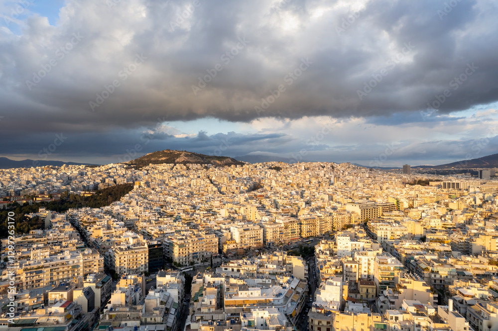 Athens aerial view over Eksarhia, Neapoli and Alexandras Avenue below big, dark clouds during golden hour.