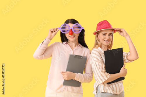Business women in funny disguise with clipboards on yellow background. April Fools' Day celebration