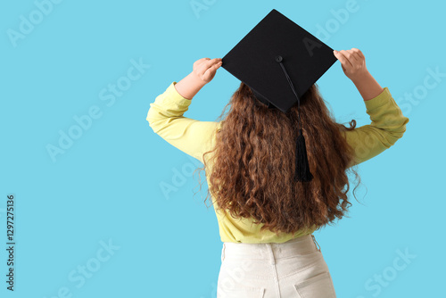 Female student in graduation hat on blue background, back view photo